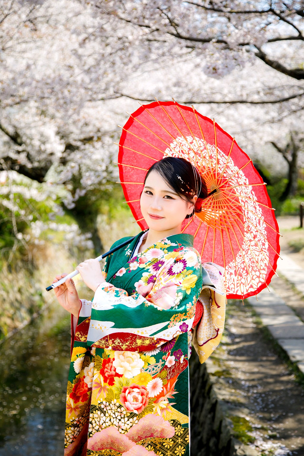 桜の下で赤い和傘を持つ着物姿